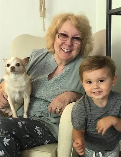 Dr. Faye Snyder smiling in a cream armchair, a small chihuahua on her lap and a smiling toddler leaning beside her